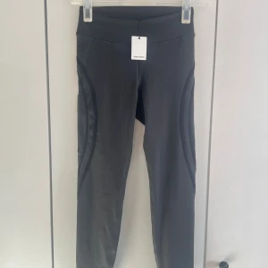 Gråa tights från Better Bodies - Snygga mörkgråa träningstights från Better Bodies med diskreta svarta detaljer längs benen och logga på baksidan. Hög midja och stretchigt material som passar perfekt för gymmet eller löpning. Tightsen har en smickrande passform och är tillverkade i funktionsmaterial. Helt nya. Innerbenslängd: 65cm 