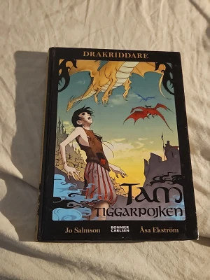 Tam Tiggarpojken - Drakriddare. författare är Jo Salmson och Åsa Ekström -  Perfekt för dig som gillar äventyr och magi. Boken är I bra skick