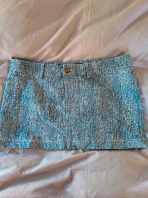 Blå jeanskjol i kort modell - Säljer en snygg blå kort jeanskjol med klassisk knappstängning och hällor för bälte. Kjolen har en tvättad denimlook och rak passform, perfekt till vardagsstilen. Inga synliga loggor eller märken.