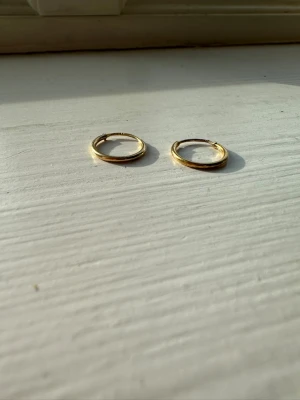 Guldfärgade hoops örhängen - Säljer ett par stilrena guldfärgade hoops örhängen i metall. De är tunna, runda och har en enkel design som passar till många olika looks. Perfekta för dig som gillar minimalistiska smycken.