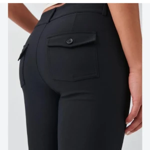 Gina Tricot Y2K kostymbyxor  - Snygga svarta byxor med bootcut passform och fickdetaljer bak. Byxorna har en klassisk look och är perfekta för dig som gillar en tidlös stil. Tillverkade i ett mjukt material som ger en bekväm känsla hela dagen.