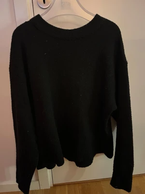 Svart stickad tröja med rund hals - En enkel och stilren svart stickad tröja med rund halsringning och långa ärmar. Tröjan har en rak passform och ribbade muddar vid ärmslut och nederkant. Perfekt basplagg för lager på lager och passar till det mesta.