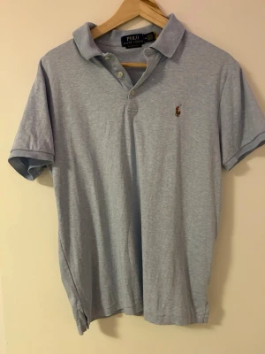 Ljusblå pikétröja från Polo Ralph Lauren - Klassisk ljusblå pikétröja från Polo Ralph Lauren med korta ärmar och krage. Tröjan har knappar framtill och den ikoniska broderade loggan på bröstet. Tillverkad i mjuk bomull för en bekväm känsla. Aldrig använd. Nypris 2199kr