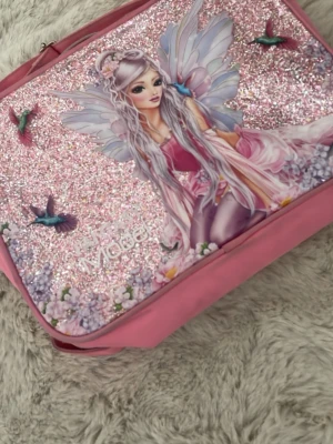 Rosa Topp modell ryggsäck - Säljer en rosa ryggsäck med glittrig framsida och ett stort älvmotiv i pastellfärger. Väskan har detaljer med blommor och fåglar, samt dragkedja upptill. Köpt för 499 men säljer för 149 då den är väldigt fläckig. Tvättas såklart innan köp 🫶🏼🫶🏼