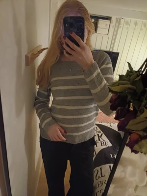 Gråvit randig stickad tröja - Mysig stickad tröja i grått med vita horisontella ränder. Tröjan har rund halsringning och långa ärmar. Perfekt för lager på lager och enkel att matcha till olika outfits.