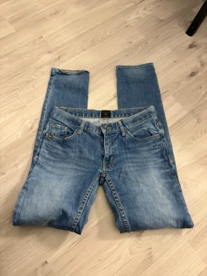 Ljusblå jeans från Tiger of Sweden - Säljer ett par klassiska ljusblå jeans från Tiger of Sweden. Jeansen har fem fickor, raka ben och snygga kontrastsömmar i gult. Perfekta till en avslappnad stil och tillverkade i mjukt denimtyg.