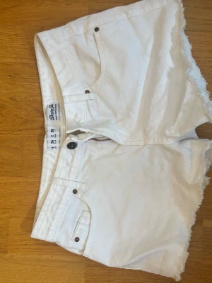 Vita högmidjade jeansshorts Bik Bok - Säljer ett par vita lågmidjade jeansshorts. Shortsen har råa kanter, fickor och stängs med knapp och dragkedja. Perfekta till sommaren och lätta att matcha med allt.