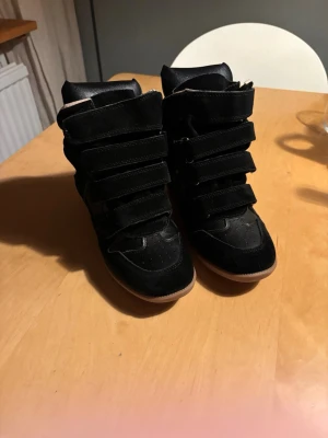 Isabel marants  - Säljer min flickväns isabel marants i storlek 38. Snygga svarta high top sneakers med flera kardborreband och brun sula. Skorna har en cool mix av mocka och skinnliknande material som ger en trendig look. Perfekta för dig som vill sticka ut och gillar streetstyle. De är nästintill orörda bara testade ett par gånger.