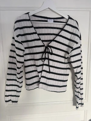 Randig stickad tröja  - Säljer en vit stickad tröja från med svarta ränder. Tröjan har v-ringning, knytband framtill och långa ärmar💞