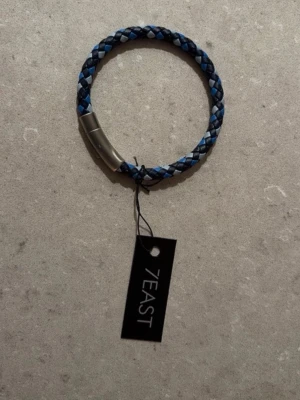Blått flätat armband från 7EAST - Snyggt armband från 7EAST i blått och svart flätat läder med ett stilrent magnetlås i metall. Perfekt accessoar för dig som vill ha en cool och enkel detalj till din outfit. Passar både till jeans och t-shirt eller skjorta.