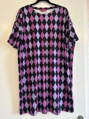 Lila och svart rutig shirtklänning - Unik med rutigt mönster i svart, lila och rosa. Modellen har rund halsringning och korta ärmar. Perfekt för dig som vill sticka ut med färg och mönster.