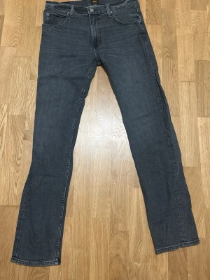 Mörkgrå raka jeans - Snygga mörkgråa jeans från Lee med rak passform och klassisk femficksdesign. Jeansen har normal midja och är tillverkade i ett mjukt denimtyg som ger en avslappnad look. Perfekta att matcha med en enkel T-shirt eller hoodie för en stilren och ledig stil. Jeansen är använda några gånger och är i fint skick.                     Storlek: W32/L34.