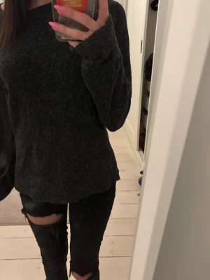 Mörkgrå stickad tröja - Mysig mörkgrå stickad tröja med avslappnad passform och långa ärmar. Tröjan har en enkel design utan synliga mönster eller detaljer och är perfekt för lager på lager. Materialet ser mjukt och bekvämt ut, perfekt för kyligare dagar.