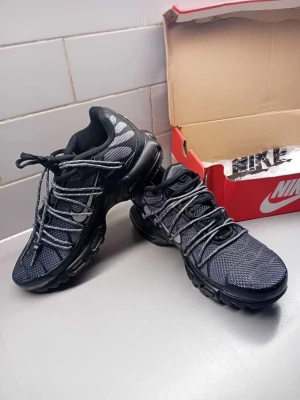 Nike svarta Air Max sneakers - Nike Air Max sneakers i svart mesh och syntetmaterial med reflekterande detaljer och synlig Air-sula. Skorna har lågt skaft, mönstrade snören och en sportig vibe. Perfekta för dig som gillar streetwear och vill ha något bekvämt och stilrent.