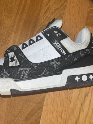 Louis Vuitton svartvita sneakers - Snygga Louis Vuitton sneakers i svart och vitt med klassiskt monogrammönster på textilen och detaljer i läder. Tydlig logga på sidan och sulan. Skorna har en chunky sula och coola kontrastdetaljer som ger en lyxig streetwear-vibe.