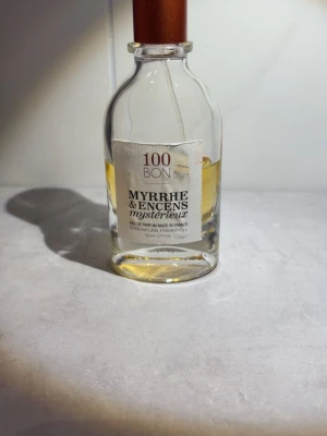 100BON Myrrhe & Encens Mystérieux parfym - En elegant parfym från 100BON, Myrrhe & Encens Mystérieux, i en genomskinlig glasflaska med kopparfärgat lock. Doften har mystiska toner av myrra och rökelse. Ungefär halva kvar!