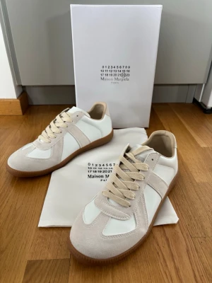 Maison Margiela sneakers beige/vit - Maison Margiela Replica sneakers i beige mocka och vitt läder med klassisk gummisula. Snygg retrostil med beige snören och diskreta detaljer. Perfekta för dig som gillar minimalistisk och stilren design.