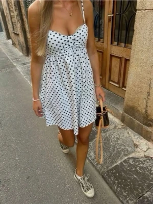 Prickig Zara klänning - Supersöt vit kort klänning med svarta prickar och smala axelband. Perfekt för sommar dagar och ger en fräsch och trendig look.
