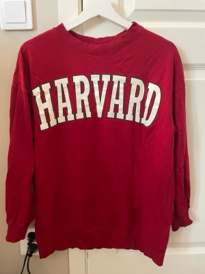 Röd sweatshirt - Röd sweatshirt med stort vitt HARVARD-tryck på bröstet. Tröjan har rund halsringning och långa ärmar. Materialet är mjukt och bekvämt, passar till jeans eller som hemmatröja bara. 