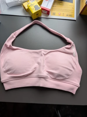 DYNE set - Ljusrosa sport-bh från DYNE med breda axelband och ribbad kant nedtill. Bh:n är sömlös och har lätt vadderade kupor för extra komfort. Materialet är mjukt och stretchigt, perfekt för en aktiv livsstil.