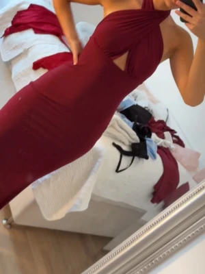 Vinröd långklänning med halterneck - Säljer en vinröd långklänning med halterneck och snygg cut-out detalj framtill. Klänningen är figurnära och har en elegant, slitsad nederdel. Perfekt för dig som vill sticka ut med en stilren och trendig look. Storlek Xs, använd endast 1 gång, lång ända ner till fötterna på mig som är 164 cm med 6 cm klackar