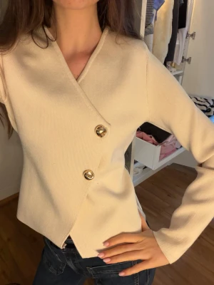 Beige omlottkofta med guldknappar - Stilren beige omlottkofta med två dekorativa guldfärgade knappar framtill. Perfekt att matcha med jeans eller kjol för en trendig look💕💕💕 helt ny