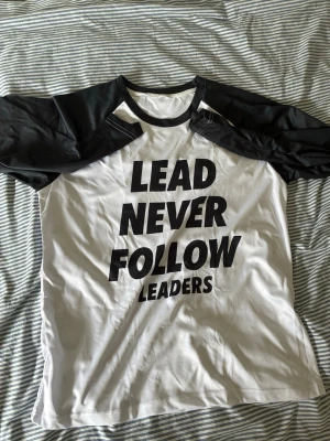 chief keef shirt - Cool svartvit t-shirt med kontrasterande svarta ärmar och stor text på framsidan: 'LEAD NEVER FOLLOW LEADERS'. Perfekt för dig som gillar statement-plagg och vill sticka ut. Klassisk passform och rund halsringning. i Storlek L