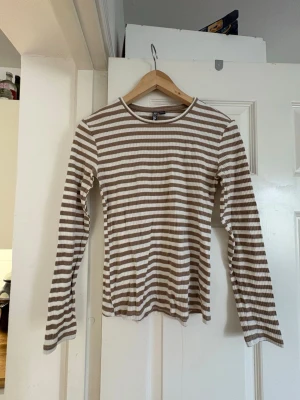 Beige och vit randig ribbad topp - Randig långärmad topp från Pisces i beige och vitt. Ribbad struktur och rund halsringning. 