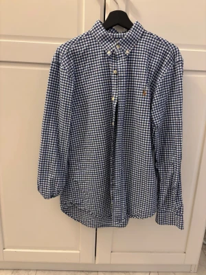 Blårutig skjorta från Polo Ralph Lauren - Snygg blårutig skjorta från Polo Ralph Lauren i slim fit-modell. Skjortan har klassisk krage, knappar framtill och lång ärm. Tillverkad i mjuk bomull och har den ikoniska loggan broderad på bröstet.