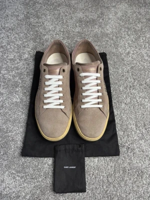 Saint Laurent skor  - Säljer nu mina ikoniska sneakers från Saint Laurent! Modellen är den extremt populära SL/06 i en fantastisk taupe/beige färg i lyxig mocka. Den perfekta blandningen av high-fashion och streetstyle! 🇫🇷🔥 Detaljer: • Märke: Saint Laurent Paris 🕊️ • Modell: Court Classic SL/06 • Material: Premium mocka med snygga läderdetaljer på hälen 🤌 • Färg: Taupe (Grå-beige) – passar till precis allt! 🎨 • Storlek: 44 📏 • Nypris: Ca 6 000 – 7 000 kr i butik 💸 • Skick: Riktigt fint skick 