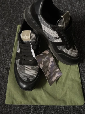 Valentino Garavani Rockrunner  - Snygga Valentino Garavani Rockrunner sneakers i svart och grått med camouflagemönster. Skorna har svarta snören, detaljer i mocka och skinn samt en robust sula med nitar baktill. Perfekta för dig som vill sticka ut med exklusiva och trendiga sneakers.