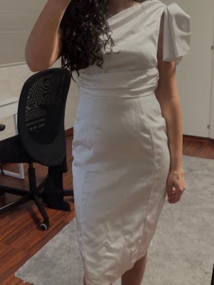 Studentklänning  - Säljer en elegant vit oneshoulder klänning med draperad midja och unik axeldetalj, med en liten slits där bak. Storlek 36. Endast använd en gång.