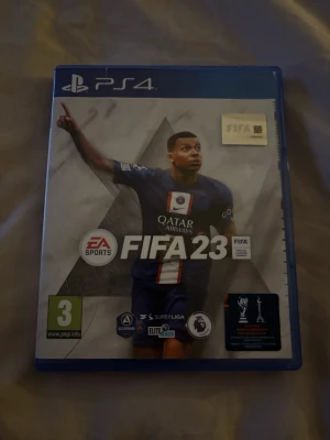 FIFA 23 till PS4 - Säljer FIFA 23 till PlayStation 4. Spelet kommer i ett blått plastfodral med omslag och matchande skiva. Omslaget har sportig design med fotbollstema och loggor från olika ligor. Perfekt för dig som gillar fotbollsspel och vill spela med vänner.