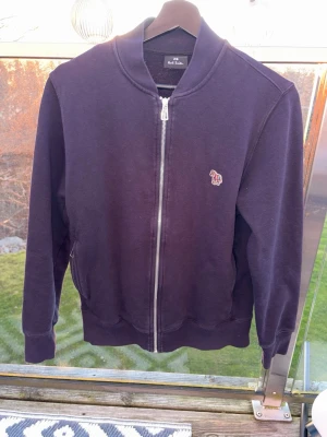 Mörkblå ziptröja från Paul Smith - Snygg mörklila ziptröja från Paul Smith med liten broderad logga på bröstet. Tröjan har ribbade muddar, ståkrage och dragkedja framtill. Perfekt för lager på lager och enkel att matcha med jeans eller byxor. Storlek S och passar S/XS, tröjan är nästan aldrig använd och har inga skador osv. Skriv vid minsta fundering🙌🏻🙌🏻