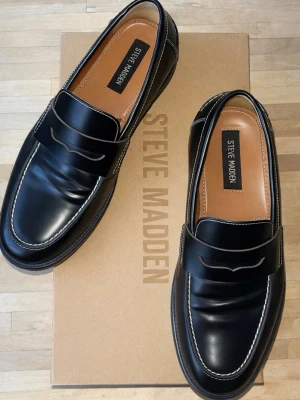 Svarta loafers från Steve Madden - Steve Madden ”Natan” loafers I äkta skinn Färg: black box Strl: 40  Använda i ca 2 veckor endast inomhus   Nypris: 1919 kr  Klassisk penny loafer-modell med markerade kontrastsömmar, låg klack och rundad tå.
