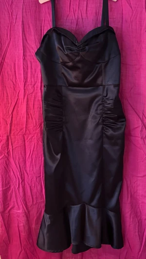 Aftonklänning Stop staring - Fin, glansig aftonklänning i retrostil från märket Stop staring. Vadlång, smickrande sjöjungfruform. Axelband, dragkedja bak. 90 % poly 10 % lycra strl XL (byst 101 cm., midja 76, höft 109) Kemtvätt. Använd en gång. 