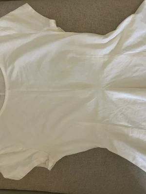 Vit basic t-shirt i bomull - En enkel och klassisk vit t-shirt med rund hals och korta ärmar och utsvängd där nere. Perfekt för att matcha med jeans eller shorts. Materialet är mjukt och känns skönt mot huden. Passformen är normal och t-shirten är helt utan mönster eller detaljer.