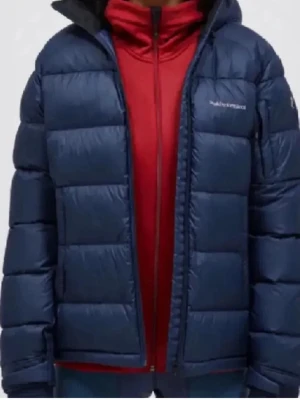 Blå dunjacka från Peak Performance -  Jag kan sänka priset.Säljer en blå dunjacka från Peak Performance med huva och quiltad design. Jackan har dragkedja framtill och logotyp på bröstet. Perfekt för kalla vinterdagar och håller dig varm med sitt dunfyllda material. Stilren och sportig look som funkar till många outfits.