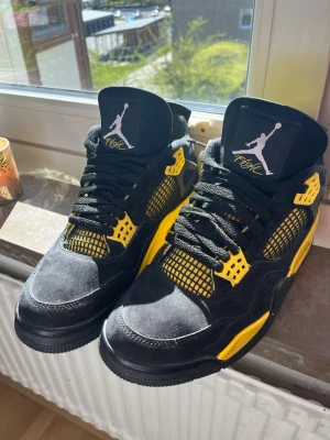 Air Jordan 4 Retro svart/gul - Säljer ett par Air Jordan 4 Retro sneakers i svart och gult med klassisk Jumpman-logga på tungan och sulan. Skorna har meshpaneler, läderdetaljer och plastdetaljer vid snörningen. Perfekt för dig som vill sticka ut med en ikonisk modell.