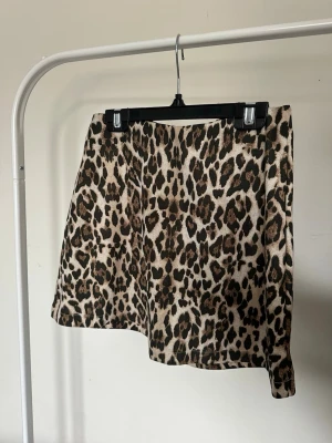 Leopardmönstrad kortkjol i beige och brun - Säljer en snygg kortkjol med leopardmönster i beige och bruna toner. Kjolen har en rak passform och är tillverkad i ett mjukt tyg som känns skönt mot huden. Perfekt för dig som vill sticka ut lite extra.