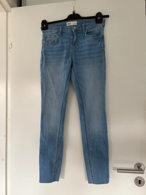 Ljusblå raka jeans från Zara - Säljer ett par ljusblå jeans från Zara med rak passform och klassisk femficksdesign. Jeansen har normal midja, dragkedja och knapp framtill samt snygga kontrastsömmar. Perfekta till en avslappnad look. Knappt använda 