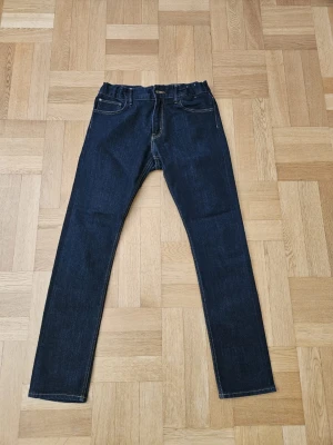 Mörkblå raka jeans med resår - Säljer ett par mörkblå jeans med raka ben och resår i midjan. Klassisk femficksdesign med kontrastsömmar och bakfickor. Perfekta för dig som gillar enkel och stilren denim-look.