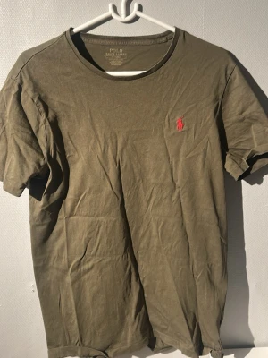 Olivgrön t-shirt från Polo Ralph Lauren - Snygg olivgrön t-shirt från Polo Ralph Lauren med klassisk röd logga. Tröjan är storlek M. Den har inga difekter eller missfärgningar på sig. Skorv vid funderingar eller pris!!
