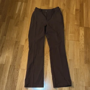 Bruna kostymbyxor från BikBok - Snygga bruna kostymbyxor från BikBok i rak modell. Byxorna har hög midja, hällor för bälte och klassisk stängning fram, är i modellen Vilma💗. Perfekta för en clean och stilren look. Materialet är mjukt och följsamt, vilket gör dem bekväma hela dagen. Stl 38, Pris 200 kr. Använd endast fåtal gånger. Kom gärna med bud💓