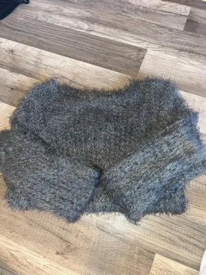 Grå fluffig stickad tröja - Mysig grå stickad tröja med fluffig, lurvig textur och rund hals. Tröjan har långa ärmar och en avslappnad passform, perfekt för att hålla värmen under kyliga dagar.  Nästan aldrig använd. Passar storlek xs- m , kontakta mig om du har frågor . 