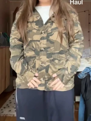 Camouflage jacka med knappar - Säljer en grön och beige camouflage jacka med knappar framtill och två stora fickor. 