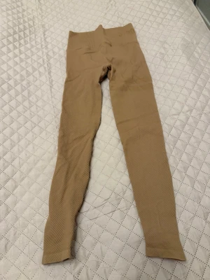Beige ribbade leggings Stronger - Säljer ett par beige ribbade leggings från Stronger med hög midja och stretchigt material. Perfekta för träning eller chill dagar. Snygg passform och diskret logga i midjan. Supersköna och trendiga!