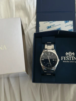 Klassisk silverklocka från Festina - Stilren klocka från Festina med mörkblå urtavla och datumvisning. Armbandet är i silverfärgat metall och klockan har en klassisk rund form. Perfekt accessoar för dig som gillar tidlös design och enkel elegans. Nypris 999kr