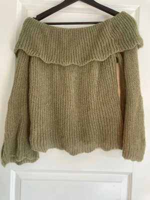 Olivgrön stickad offshoulder tröja - Säljer en olivgrön stickad tröja med bred offshoulder-krage. Tröjan har grov ribbstickning och långa ärmar med lite loose passform. Perfekt för dig som gillar chill och snygg stil med en twist. Materialet är mjukt och värmande stickat garn.