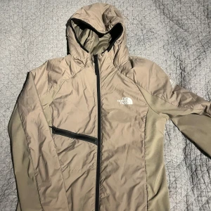 Beige vindjacka från The North Face - Snygg beige vind/ vinterjacka från The North Face. Extremt bra passform, den är i Storlek Small. Den ser endast skrynklig ut på bilden eftersom ingen bär den, skriv privat om du vill ha en bild med jackan på. Använd ett fåtal gånger, originalpris: 1 745 kr